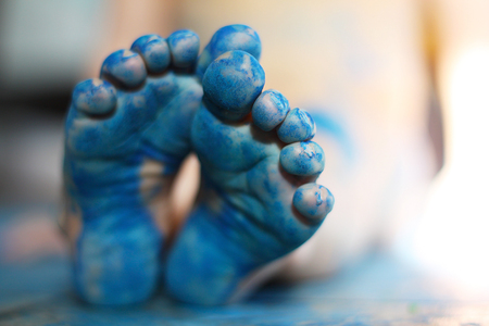 a close up on the bottom of the feet of a small child, that have been painted blue.  Very shallow depth of field with focus on toes of front foot.の写真素材