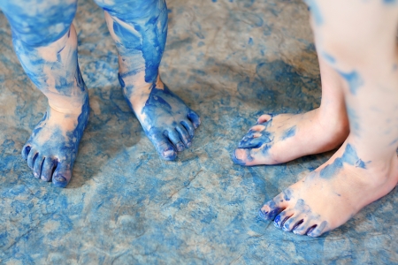 two pairs of very messy blue painted kid's feet are standing on a floor covered in paintの写真素材