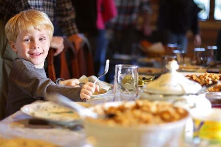 a happy young child is smiling as he sits at the holiday dinner table with a fork and plate, waiting for his mealの写真素材