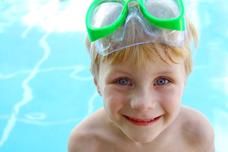 a little child is smiling as he stands by the swimming pool with goggles on his headの写真素材