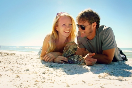 an attractive, happy young couple is laying on the beach next to the ocean, smilingの写真素材