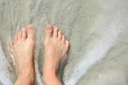 close up portrait of a woman's feet standing on the beach shore as the ocean waves wash over themの写真素材
