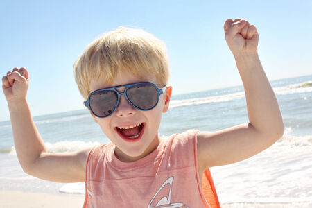 a happy young child is holding up his fists and flexing his muscles on the beach in front of the...