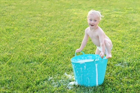 A cute baby boy is making a funny face as he plays outside with bubble soap and water in a wash tub on a summer day の写真素材