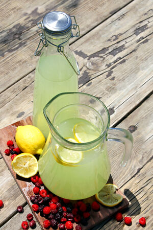 Two pitchers of fresh squeezed lemonade are sitting outside on a rustic wood picnic table surrounded by Raspberry fruit on a summer day,の写真素材