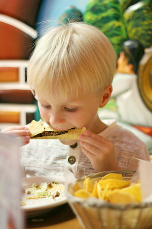 A young Caucasian boy is eating a beef hard shell Taco at a Mexican Restaurant.の写真素材