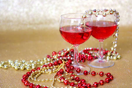 Two wine glasses filled with a red drink are surrounded by bright beaded New Years Eve necklaces in front of a glittery gold の写真素材
