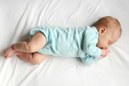 A precious newborn infant is laying on a comfortable white bed, sleeping peacefully.の写真素材
