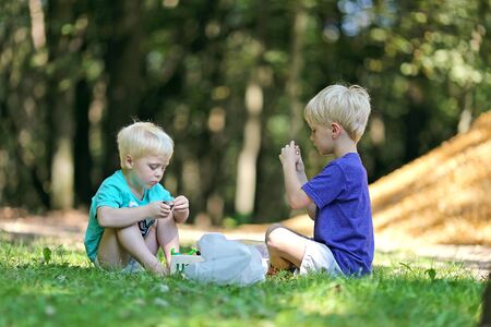 Two little boys are playing outside in the woods, with toys and dirt on a summer day.の写真素材