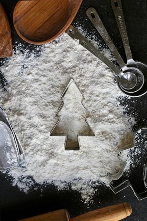 A silver metal Christmas Tree cookie cutter is sitting in a pile of spilled white baking flour, framed by a variety of wood and steel vintage cooking supplies and utensils.の写真素材