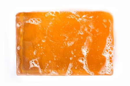 An orange bar of glycerin face soap with suds on it is isolated on a white background.