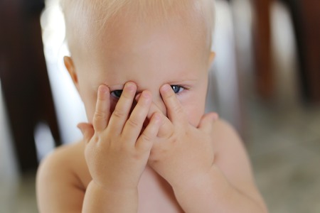 A one year old baby girl is covering her face with her hands and peeking through her fingers.の写真素材
