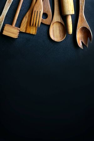 A collection of vintage wooden cooking utensils, spoons, rolling pin, masher, spatula, are framing the top border of a black slate chalkboard.の写真素材