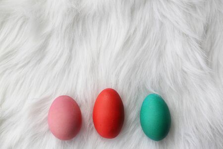 Three Easter Eggs painted in different pastel colors are lined up on the bottom border of a furry white background.の写真素材