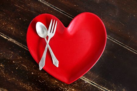 An empty red heart shaped dinner plate with a silver spoon and fork is sitting on an old worn out...