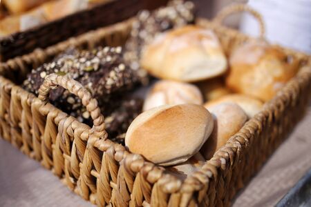 A display of fresh baked dark rye and hard roll breads are displayed in a wicker woven basket at an...