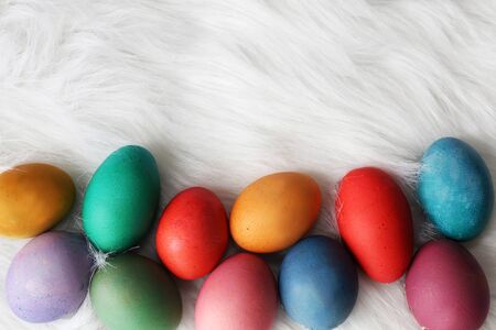 A variety of different colored and sized painted easter eggs are framing the bottom border of a fur...