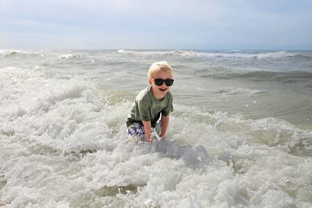 A happy and smiling little child is laughing as he splashes in the ocean waves on a summer day at...