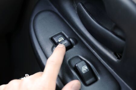 The hand of a woman is pressing the lock door button from the interior of her car.の写真素材