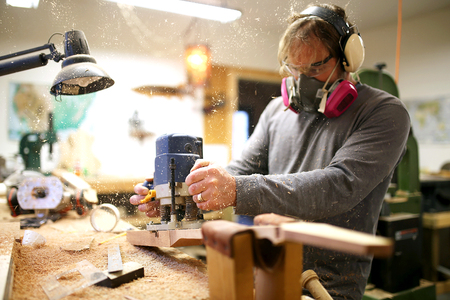 A Wood working luthier man is using a plunge router tool to build a guitar in his home workshopの写真素材