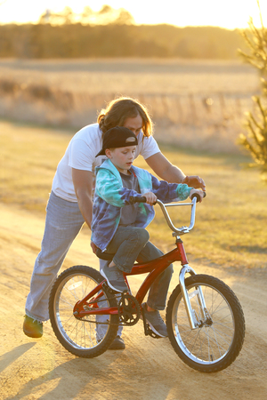 A father is helping his young child learn to ride his bike on a sunny spring evening.の写真素材