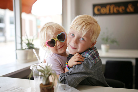 A sweet little boy child is hugging his cute baby sister as the sit at a table in a coffee house Bakery.の写真素材