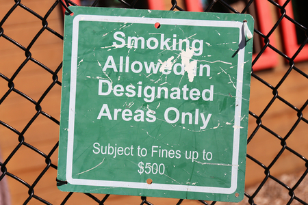 A green sign is hung on a chain link fence at a playground, and says "Smoking allowed in designated areas only, $500 fine".の写真素材