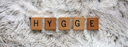 The Danish word Hygge is is spelled out on wooden word blocks and resting on a soft and cozy white faux fur blanket. Sized for Social Media Cover photo.の写真素材