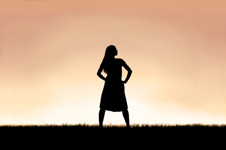 The silhouette of a strong, beautiful woman stands isolated against a sunset in the sky background.の写真素材