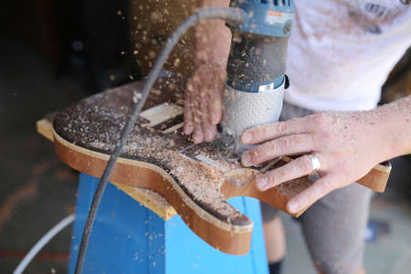 A Luthier is using a power Dremmel tool to drill shapes in to a handmade wooden electric guitar that he is building.の写真素材