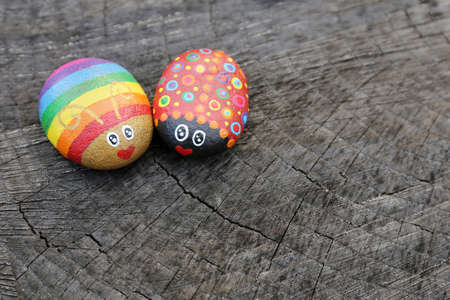 Two hand painted rainbow love bugs on rocks are sitting on a natural wood background.の写真素材