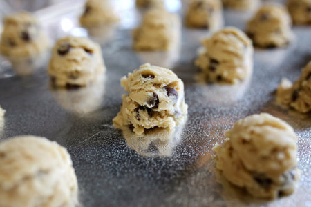 A tray lined with aluminum foil and greased is full of homemade chocolate chip cookies rolled from...