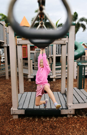 Happy Little Girl Child Swinging on Monkey Bar Rings at Playgroundの写真素材