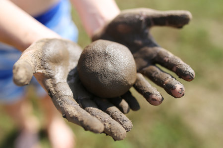 A closeup of a child playing outside with a ball of clay rolled up in his muddy hands.の写真素材