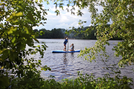 Two little girl children are riding on a paddle board on a lake on a summer day.の写真素材