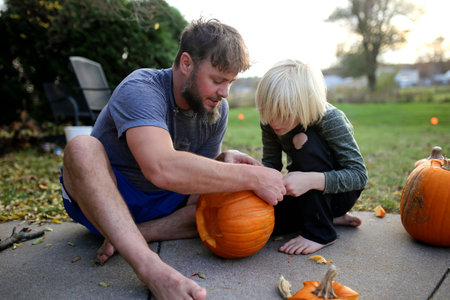 A father is helping his young son carve a pumpkin for Halloween.の写真素材