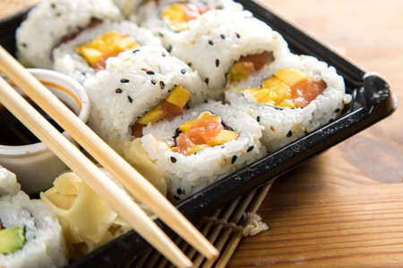 Salmon mango inside out California sushi with soy sauce, pickled ginger and wooden chopstick in take away Bento boxの写真素材
