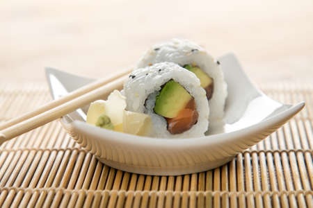 Two salmon avocado inside California sushi rolls with wasabi, pickled ginger and wooden chopsticksの写真素材