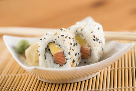 Two salmon mango inside out California sushi rolls with wasabi, pickled ginger and wooden chopsticksの写真素材
