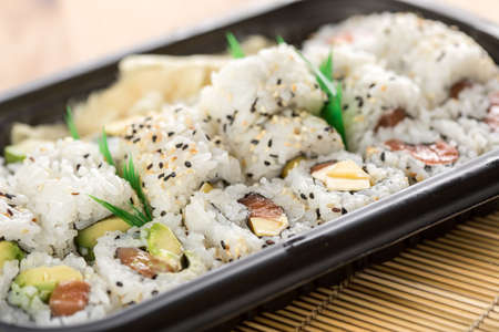 Salmon, avocado and mango inside California sushi with soy sauce, pickled ginger and wooden chopstick in take away Bento boxの写真素材