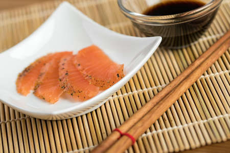 Smoked and stained salmon sashimi slices on porcelain dish with soy sauce and wooden chopsticksの写真素材