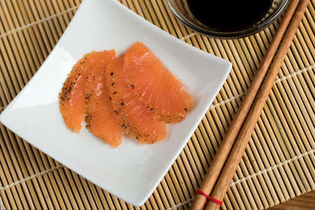Smoked and stained salmon sashimi slices on porcelain dish with soy sauce and wooden chopsticksの写真素材