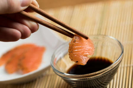 Woman dipping smoked and stained salmon sashimi slice in soy sauce using chopsticksの写真素材