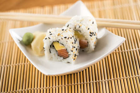Two salmon mango inside out California sushi rolls with wasabi, pickled ginger and wooden chopsticksの写真素材