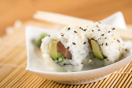 Two salmon avocado inside California sushi rolls with wasabi, pickled ginger and wooden chopsticksの写真素材