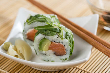 Salmon avocado rocks out of sushi with soy sauce, wasabi, pickled ginger and chopsticks
