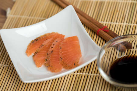 Smoked and stained salmon sashimi slices on porcelain dish with soy sauce and wooden chopsticksの写真素材