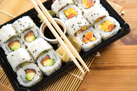 Salmon, avocado and mango inside California sushi with soy sauce, pickled ginger and wooden chopstick in take away Bento boxの写真素材