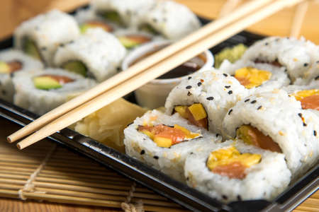 Salmon, avocado and mango inside California sushi with soy sauce, pickled ginger and wooden chopstick in take away Bento boxの写真素材