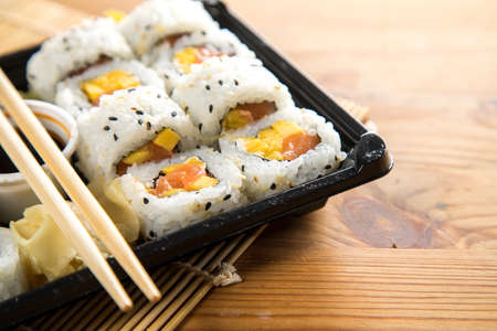 Salmon mango inside out California sushi with soy sauce, pickled ginger and wooden chopstick in take away Bento boxの写真素材